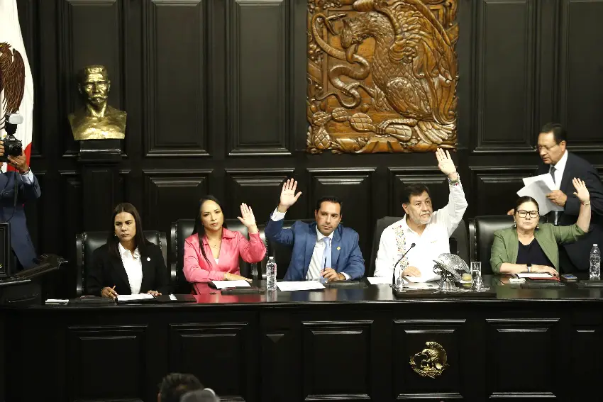 Mexican Senate President and Morena Gerardo Fernández Noroña and other senators sit at a dias and raise their hands during a Senate session.