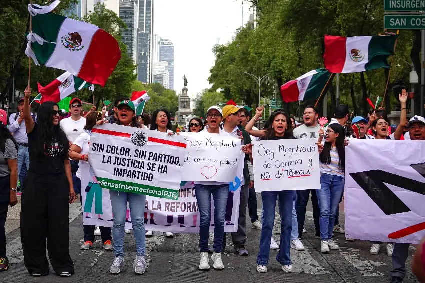 People march down a wide avenue in Mexico City, holding Mexican flags and handwritten signs