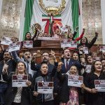 A group of Mexico City legislators standing by the head of the legislature's bench and behind it, holding signs that say "The Reform goes forward!"