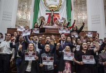 A group of Mexico City legislators standing by the head of the legislature's bench and behind it, holding signs that say "The Reform goes forward!"