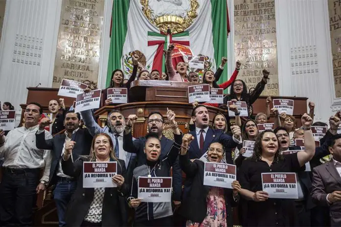 A group of Mexico City legislators standing by the head of the legislature's bench and behind it, holding signs that say 