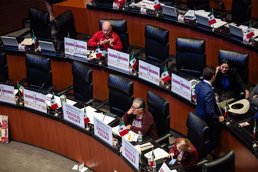 Mexican senators sitting in session with placards with slogans in Spanish in front of their seats.