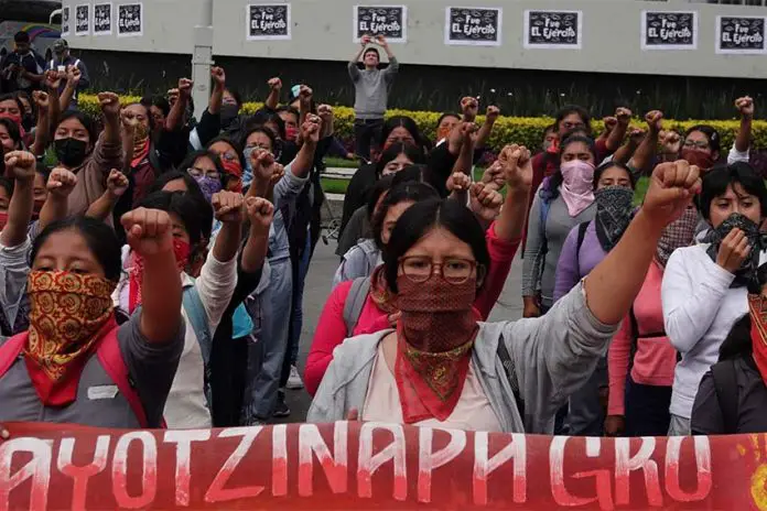 Multiple women standing in rows in a courtyard with their left fists raised in the air. Before the front row is a banner saying 