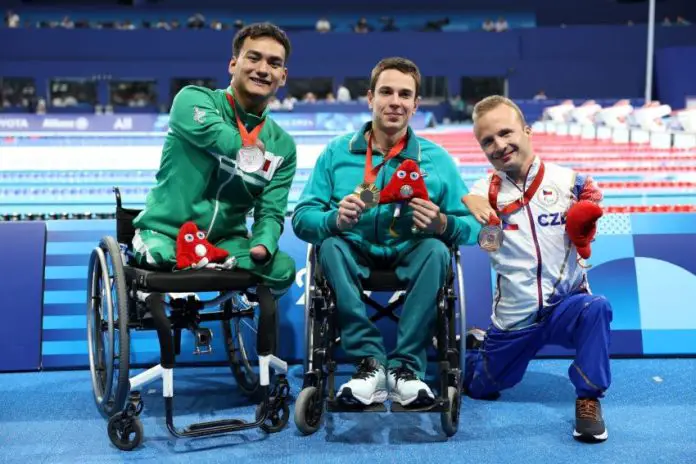 Mexican swimmer Ángel Camacho displays his medal, sitting next to the first and third place winners of the 50-meter backstroke S4 category.