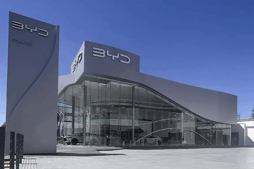 Fuera de una sala de exhibición de automóviles BYD en Guadalajara, México, con ventanas de vidrio de piso a techo en un edificio con el logotipo de BYD en letras plateadas.