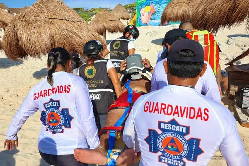 A group of six lifeguards on a beach in Mexico carrying a stretcher with an injured man in shorts and no shirt