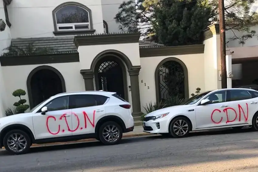 Two white sedans parked along a sidewalk, each bearing large graffiti letters saying CDN