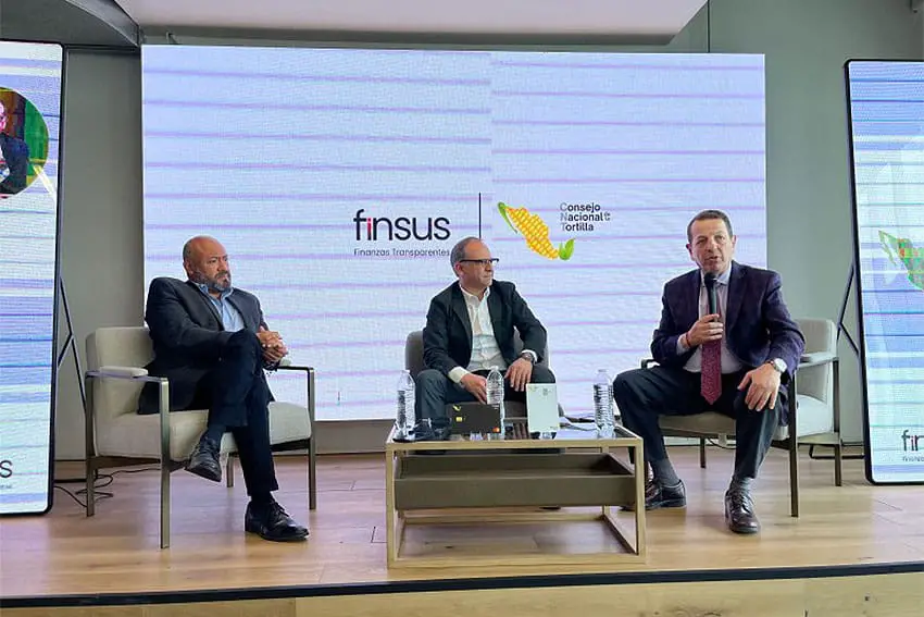 Three men seated in chairs on a small stage with the logos for Mexico's National Tortilla Council and the fintech bank Finsus on a wall in the background.