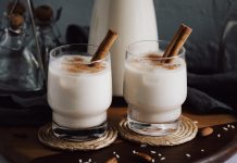 Two glasses of horchata dusted with cinammon and with cinammon sticks sticking out of them.