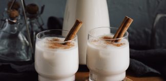 Two glasses of horchata dusted with cinammon and with cinammon sticks sticking out of them.