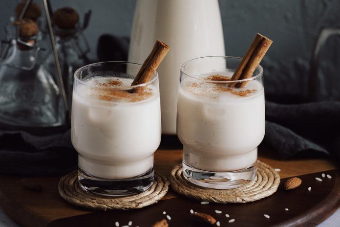 Two glasses of horchata dusted with cinammon and with cinammon sticks sticking out of them.