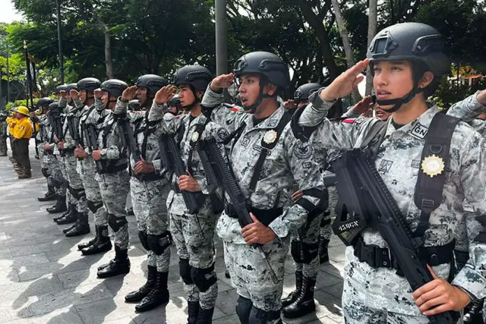 Horizontal line of Mexico's national guard members in uniform and holding guns, saluting ceremonially