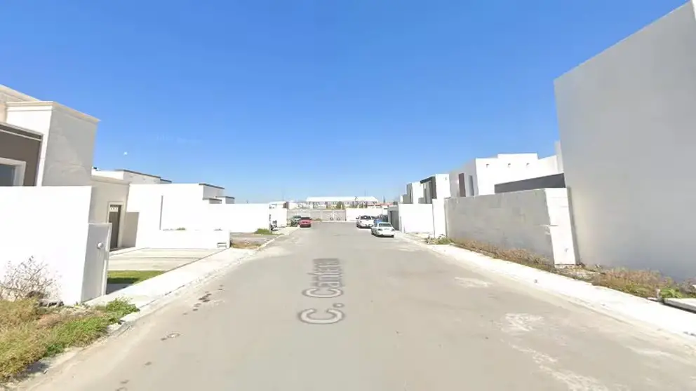 view of street in Nuevo Laredo housing development with all white homes and walls and some cars parked in the distance