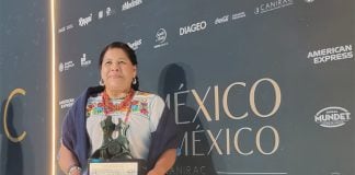 Restauranteur Rosalba Morales Bartolo poses against a backdrop of the Canirac Awards, poses for photos with her trophy. She's wearing a white, traditional indigenous blouse with handmade embroidery and a dark blue shawl.
