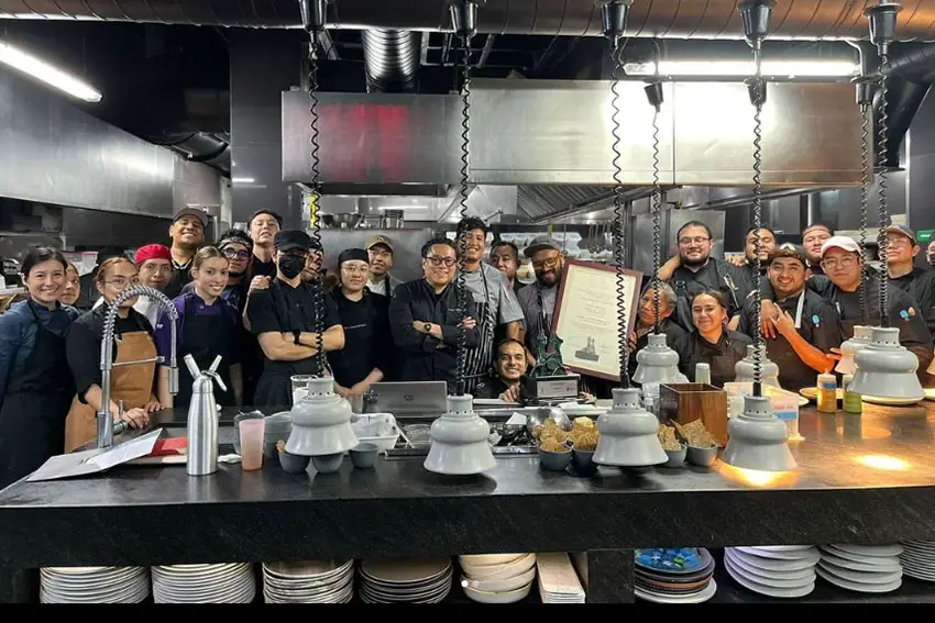 the staff of Mexico City's Balcon de Zocalo restaurant, all earing black chef's outfits, standing posed for a a group photo with Chef Pepe Salinas, who is in front center. One staff members holds up Salinas' framed award certificate from Canirac