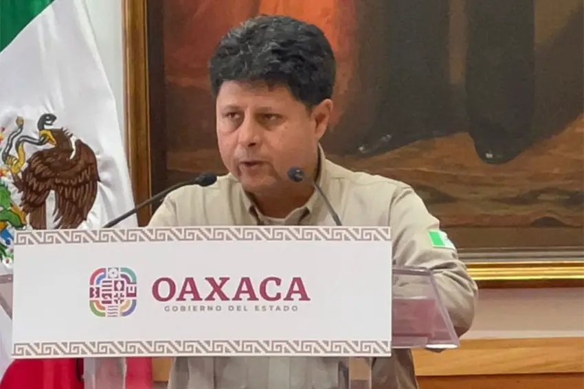 Man standing behind a podium that said State Government of Oaxaca and speaking to reporters