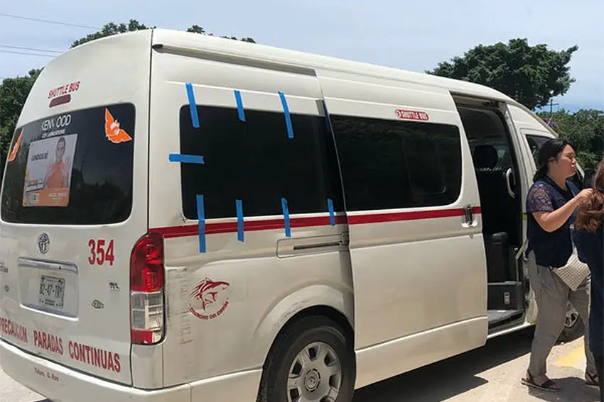 A white 15-passenger van in Tulum with people exiting it.