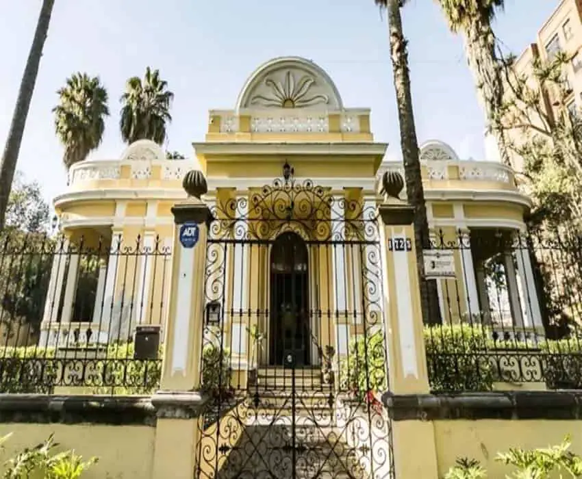 Yellow and white Renaissance revival house with columns, three turrets an arched door, a wrought-iron gate in front and a wrap-around verandah