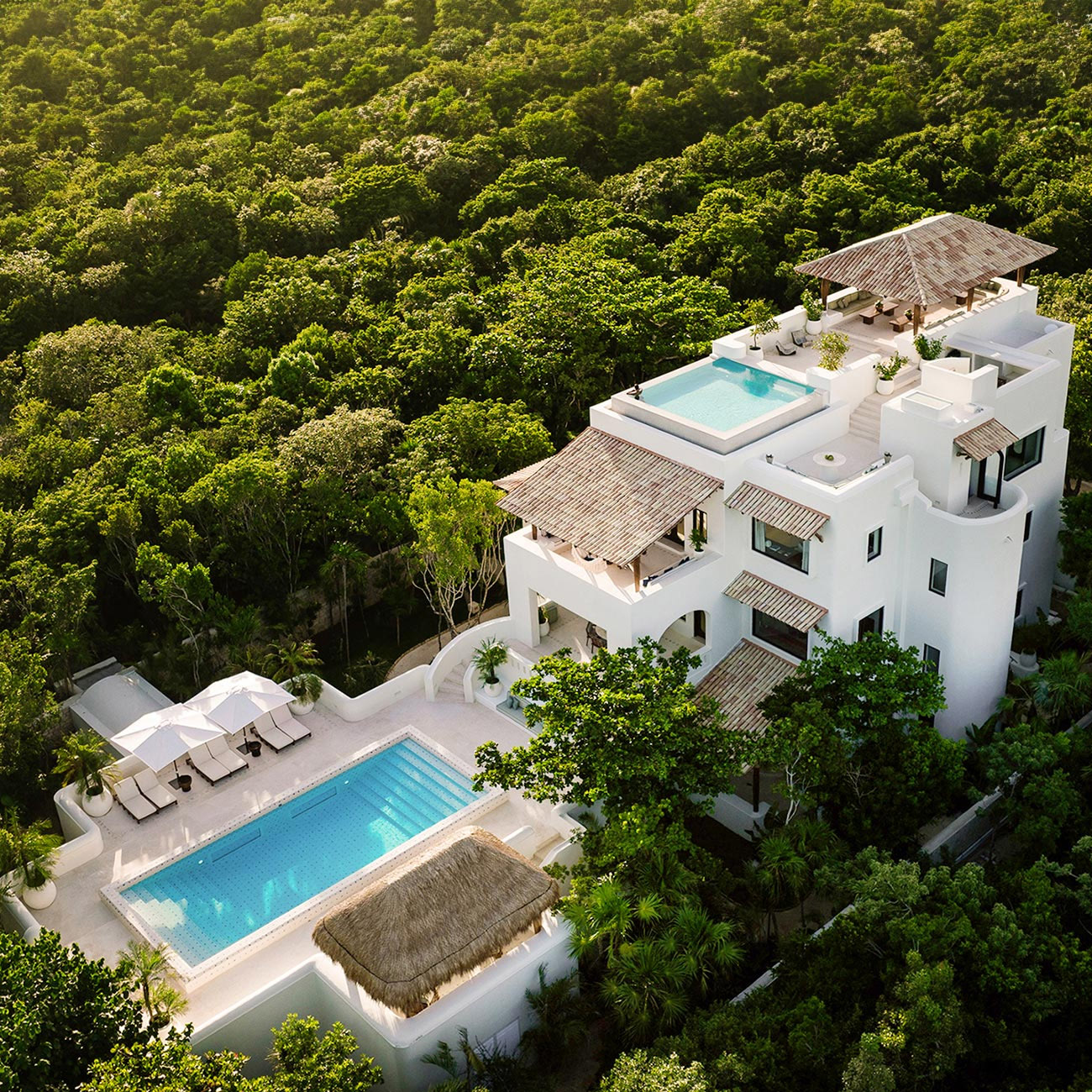 A white hotel with blue pools sits in the middle of a dense green forest in Quintana Roo, Mexico