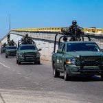 A convoy of military vehicles with armed soldiers perched on top drives down a highway in Sinaloa