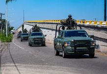 A convoy of military vehicles with armed soldiers perched on top drives down a highway in Sinaloa