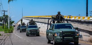 A convoy of military vehicles with armed soldiers perched on top drives down a highway in Sinaloa