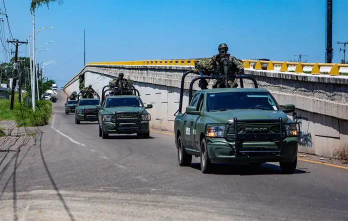 A convoy of military vehicles with armed soldiers perched on top drives down a highway in Sinaloa