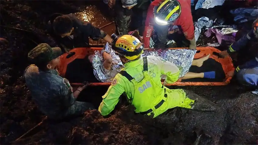 Rescuers in neon rain gear and head lamps transport a woman on a stretcher across a debris field after a mudslide in México state.