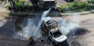 A firefighters sprays water at a smoldering truck that blocks a road in Culiacán