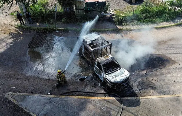 A firefighters sprays water at a smoldering truck that blocks a road in Culiacán