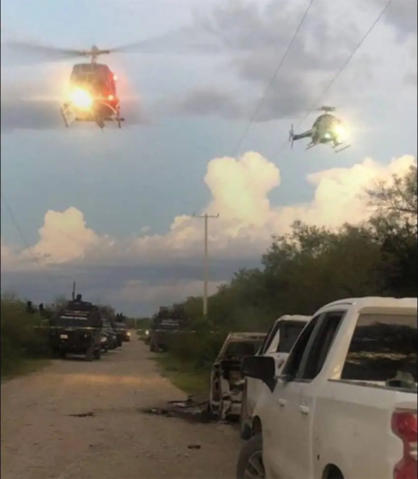 Helicopters fly over white pickup trucks on a dirt road in Nuevo León. 