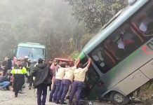 People in uniforms push on a bus that crashed on a mountainous road near Machu Picchu, Peru, while injured passengers sit and lie on the ground nearby.