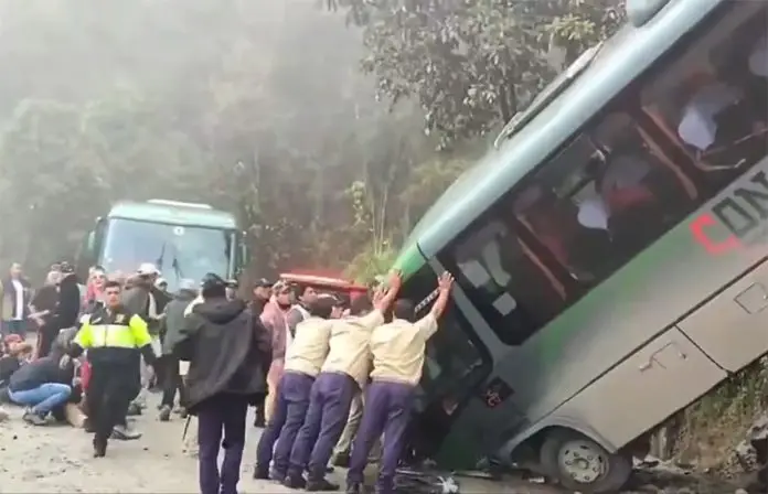 People in uniforms push on a bus that crashed on a mountainous road near Machu Picchu, Peru, while injured passengers sit and lie on the ground nearby.