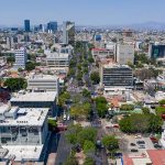 Aerial view of Colonia Americana neighborhood of Guadalajara. Skyline with multiple skyscrapers and a long avenue in the center, with a mountain range far in the background of the photo.