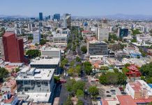 Aerial view of Colonia Americana neighborhood of Guadalajara. Skyline with multiple skyscrapers and a long avenue in the center, with a mountain range far in the background of the photo.