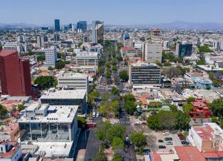 Aerial view of Colonia Americana neighborhood of Guadalajara. Skyline with multiple skyscrapers and a long avenue in the center, with a mountain range far in the background of the photo.