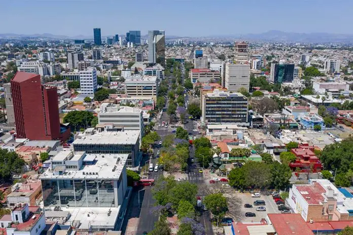 Aerial view of Colonia Americana neighborhood of Guadalajara. Skyline with multiple skyscrapers and a long avenue in the center, with a mountain range far in the background of the photo.