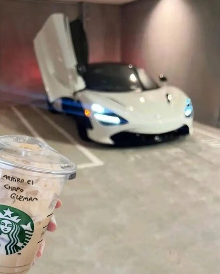 Una taza de Starbucks con las palabras "Arriba El Chapo Guzmán" con un coche de lujo al fondo