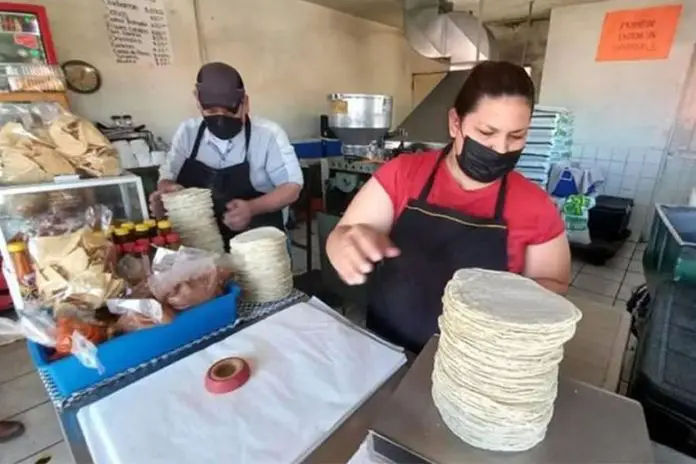 A woman tortilla vendor in Mexico weighing a large stack of tortillas