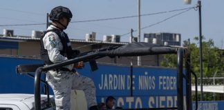 National Guardsman in uniform in a truck bed on patrol through Mexican streets.