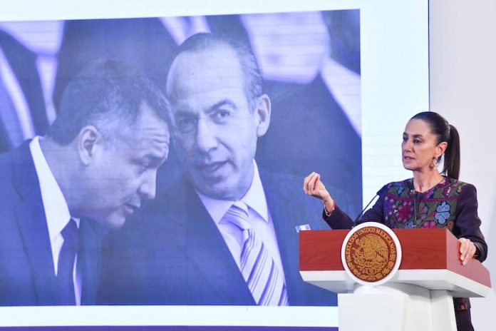 President Claudia Sheinbaum stands at a podium in front of a photo of Felipe Calderón and Genaro García Luna.