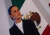 President Sheinbaum stands in front of a Mexican flag at her morning press conference