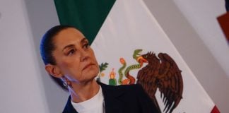 President Sheinbaum stands in front of a Mexican flag at her morning press conference