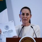 Claudia Sheinbaum at a press conference holding a copy of Mexico's Official Gazette of the Federation document