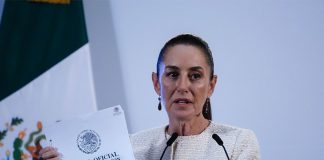 Claudia Sheinbaum at a press conference holding a copy of Mexico's Official Gazette of the Federation document