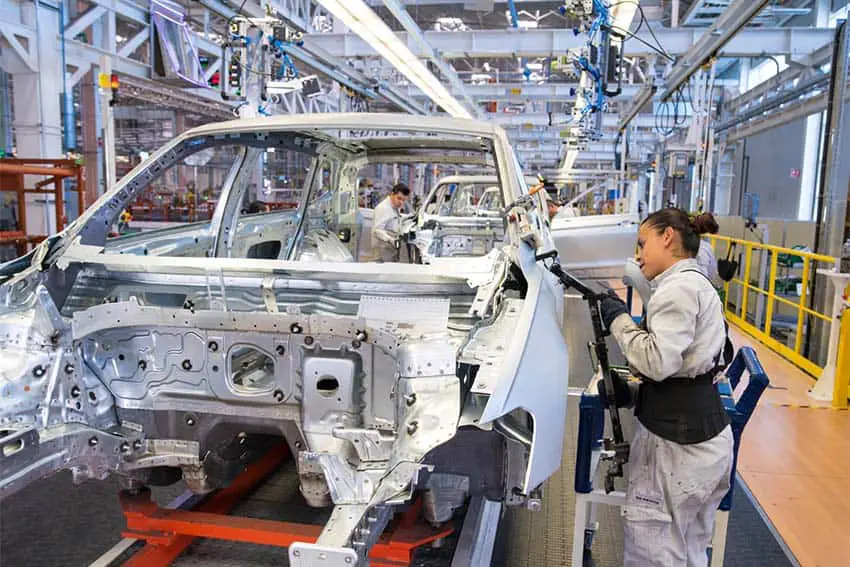 Volkswagen factory workers in Puebla, Mexico assembling a white car frame on an assembly line