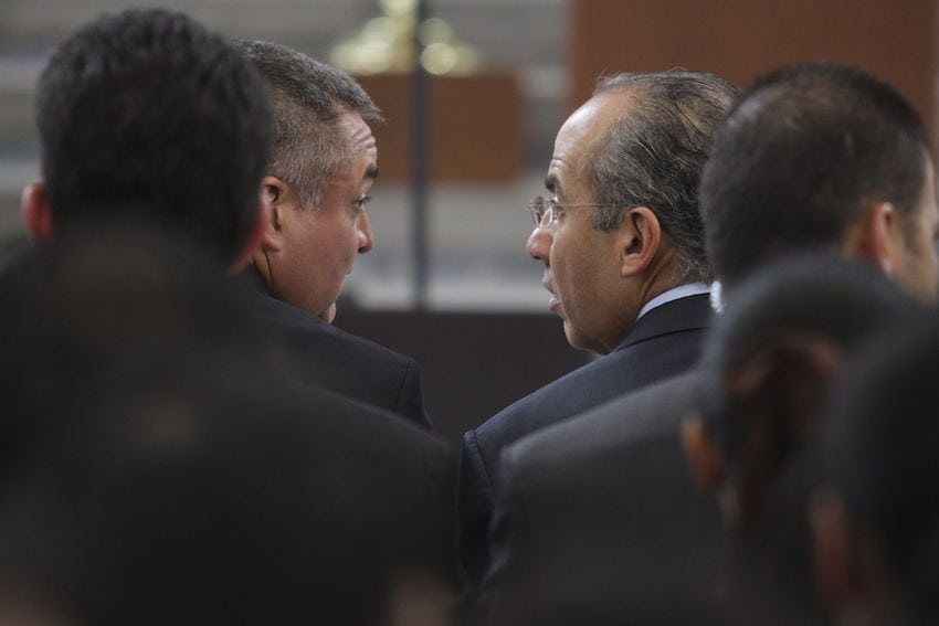 Then-Security Secretary Genaro García Luna turns in his chair to speak with former President Felipe Calderón, in a photo taken from behind.