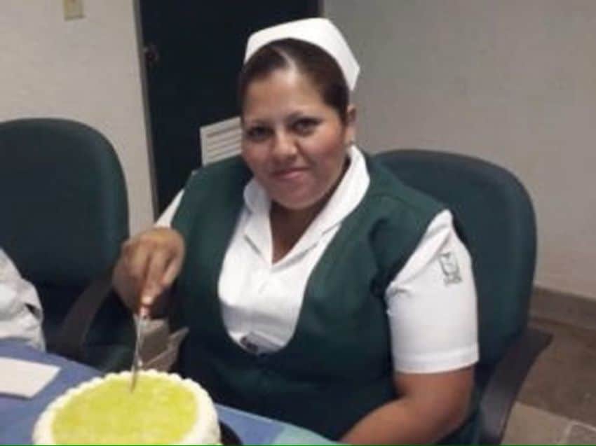 Woman in an nurse's uniform for Mexico's National Social Security Institute sits in a hospital break room cutting a decorated cake.