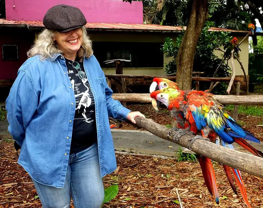 Karina Aguilar stands nexts to two macaws perched on a branch