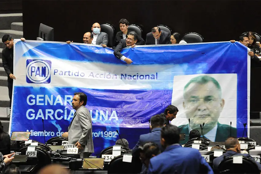 Members of Mexico's Lower House of Congress in session holding up a banner with a photo and the name of Genaro Garcia Luna with the logo of Mexico's National Action Party.